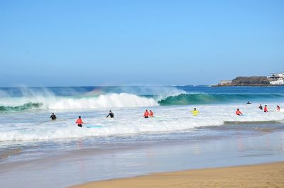 People on shore at beach against clear sky