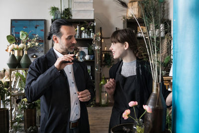 Smiling young female entrepreneur talking with mature male customer holding magnifying glass at store