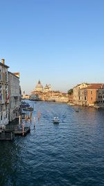 Boats in canal by buildings against clear sky