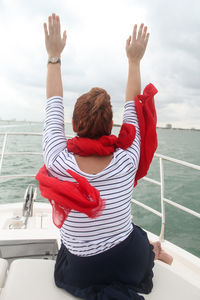 Woman enjoying yacht cruise,  luxury boat, wearing nautical clothing, red scarf, her arms are raised