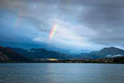 Scenic view of rainbow over lake and mountains against sky