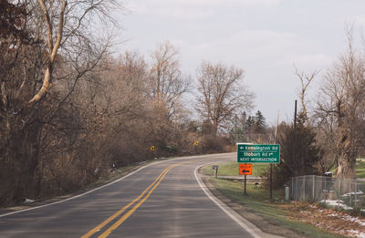 Road sign by trees against sky