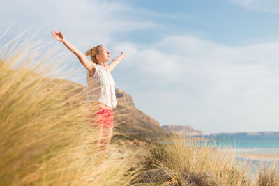 Woman with arms raised on field against sky