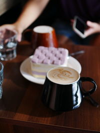 Coffee table with square shaped cake and coffee - women in background taking photo - pov