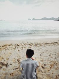 Rear view of man sitting on beach while looking at sea