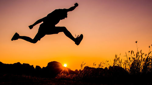 Silhouette man jumping against orange sky during sunset