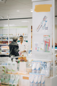 Senior female customer talking with male pharmacist at checkout in store