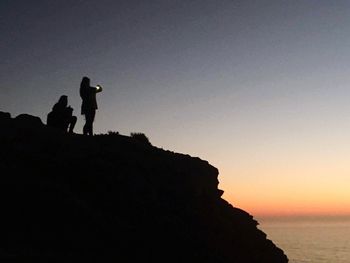 Silhouette men standing on mountain against clear sky