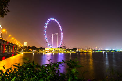 Illuminated city by river against sky at night