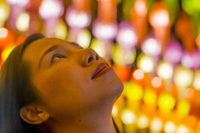 Close-up portrait of woman with illuminated eyes closed at night