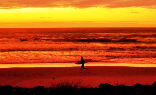 Silhouette man at beach against orange sky