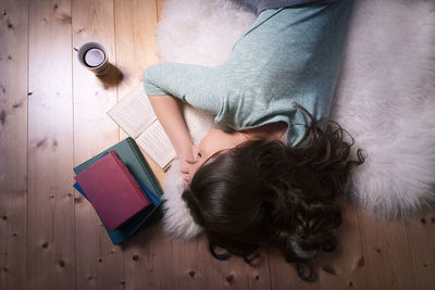 High angle view of woman with books sleeping on hardwood floor at home