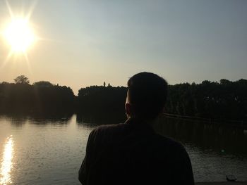 Rear view of man standing by lake against sky during sunset