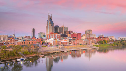 Reflection of buildings in river against sky during sunset