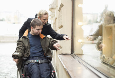 Disabled man on wheelchair widow shopping with caretaker