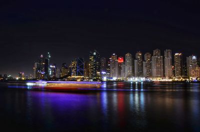 Illuminated buildings by river against sky at night