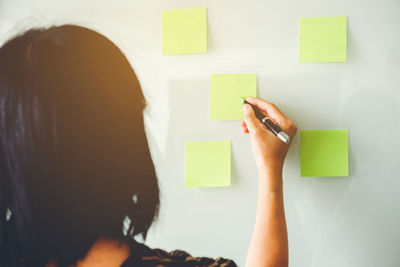 Rear view of woman writing on green adhesive notes on whiteboard