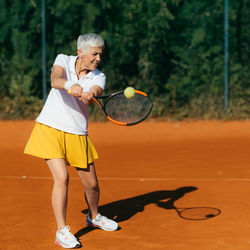 Smiling mature woman playing tennis in summer