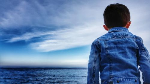 Rear view of a boy overlooking calm blue sea