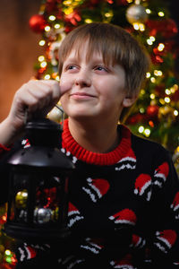 Portrait of smiling young boy sitting in front of christmas tree 