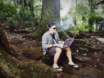 Full length of teenage girl sitting on tree trunk