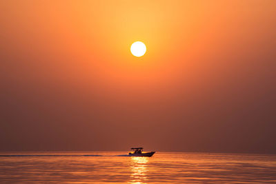 Silhouette boat sailing on sea against orange sky