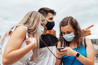 People wearing mask using smart phone standing outdoors