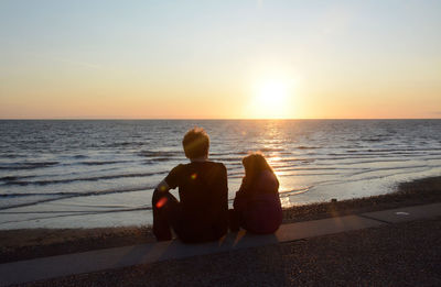 People sitting on beach against clear sky during sunset