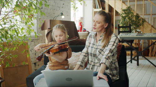 Mother teaching violin to daughter at home