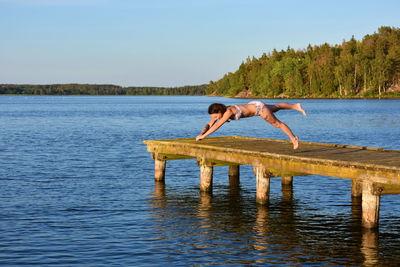 Side view of woman jumping in lake against sky