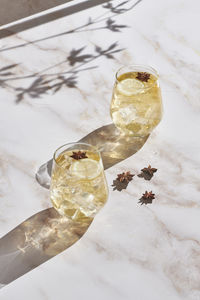 High angle of delicious cocktails with lemon slices and ice cubes garnished with star anise and served on marble table