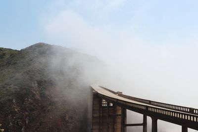 Bridge by mountain during foggy weather