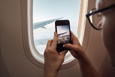 Cropped image of person photographing through airplane window