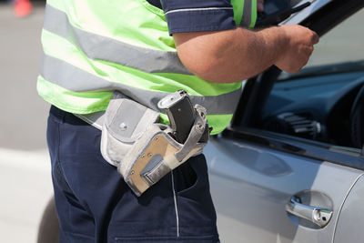 Midsection of police officer with gun standing by car