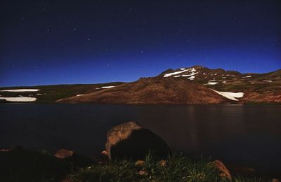 Scenic view of lake by mountain against sky at night