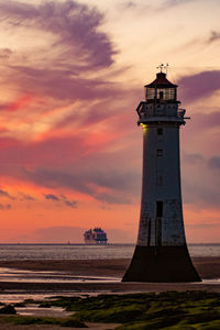 Lighthouse by sea against sky during sunset