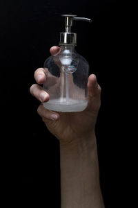 Close-up of hand holding glass bottle against black background