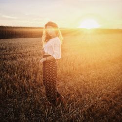 Young woman standing on field against bright sky during sunset