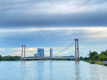 View of suspension bridge over river against cloudy sky