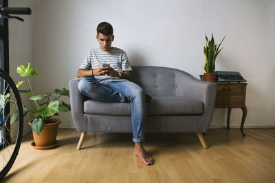 Teenage boy sitting on couch at home looking at cell phone