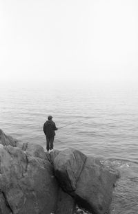 Man fishing in sea against clear sky