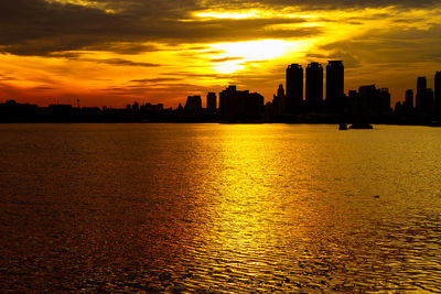 Silhouette buildings by sea against sky during sunset