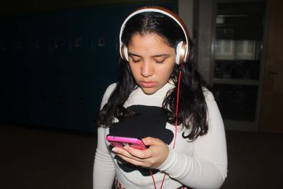 Close-up of young woman using phone while standing against black background