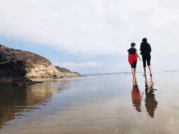 Rear view of people standing on beach against sky