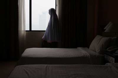 Rear view of woman standing on bed