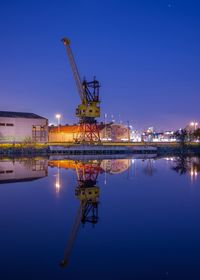 Illuminated industrial buildings and crane with reflection on lake at night