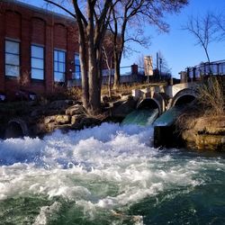 Bridge over river by buildings against sky