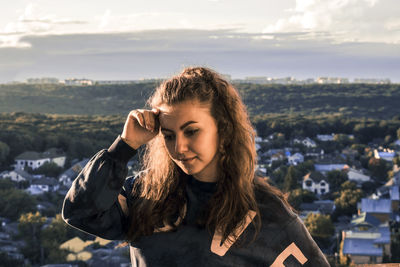 Thoughtful young woman looking down against houses