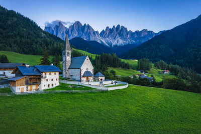Scenic view of field by houses and mountains against sky