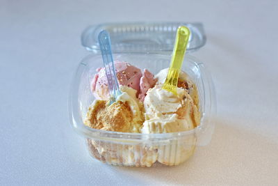 Close-up of dessert served on table -
ice creams balls in plastic box with colorful spoons for two